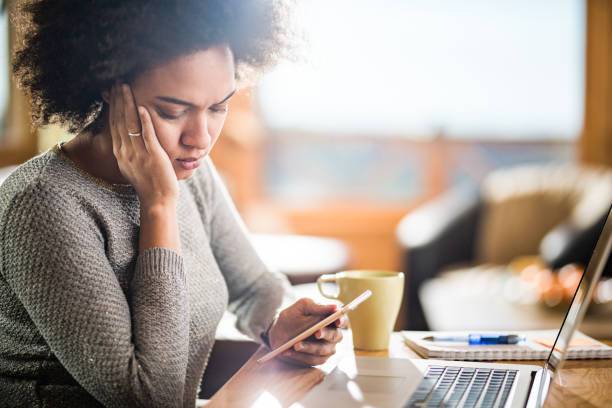istock Worried African American woman reading text message on mobile phone while working at home. 1142157155