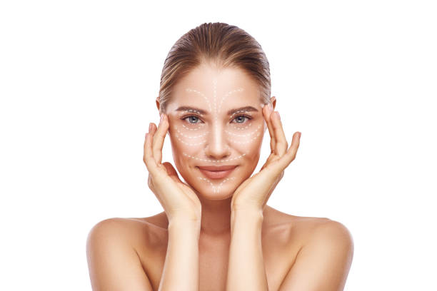 masaje facial anti-aging. hermosa mujer joven con flechas blancas sobre su cara manteniendo las manos en la cabeza y mirando a la cámara. aislado sobre fondo blanco. cuidado de la piel. líneas de masaje - wrinkle treatment fotografías e imágenes de stock