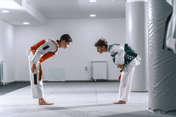 zwei kaukasische jungen in taekwondo-armaturen beugen sich nach dem kampf aneinander. - tae kwon do stock-fotos und bilder