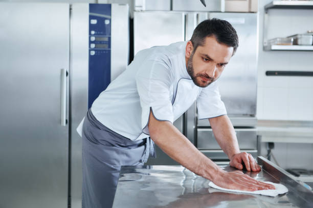 When preparing foods keep it clean, a dirty area should not be seen. Young male professional cook cleaning in commercial kitchen Bearded man prepares the surface for cooking in the kitchen. Cook carefully wipes the surface. Health and safety concept. hygiene stock pictures, royalty-free photos & images