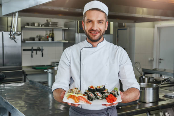 Already ready. Portrait of cheerful chef standing with cooked traditional japanese sushi stock photo