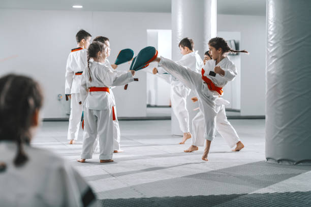 gruppo di bambini sportivi caucasici nei dobok che hanno lezione di taekwondo in palestra bianca. - tae kwon do foto e immagini stock