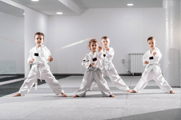 pequeño grupo de niños caucásicos en doboks practicando taekwondo y calentando para el treining mientras está parado descalzo. - taekwondo fotografías e imágenes de stock