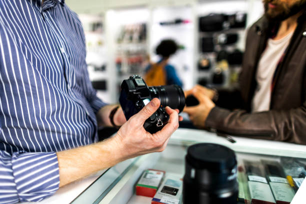 istock Camera store salesman demonstrating various camera lenses on a mirrorless camera to his customer in a camera shop 1142175406