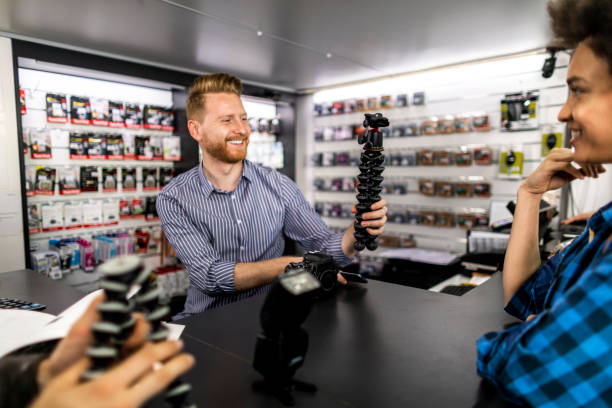 istock Store retailer holding a vlogging camera tripod stand for a DSLR camera at the checkout counter for an interested couple in a camera accessories store 1142175743