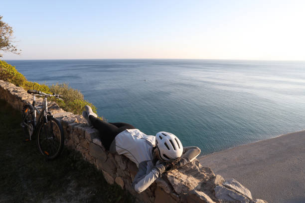 female cyclist relaxes on rock wall above the sea - beach stone wall one person imagens e fotografias de stock