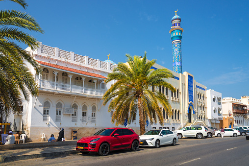 Muscat, Oman - March, 17. 2019 - Al Bahri Road im Muscat - Oman with view to the mountains with minaret and parking modern cars. Local people walking in the street. The mosque called Masjid Al Rasool.