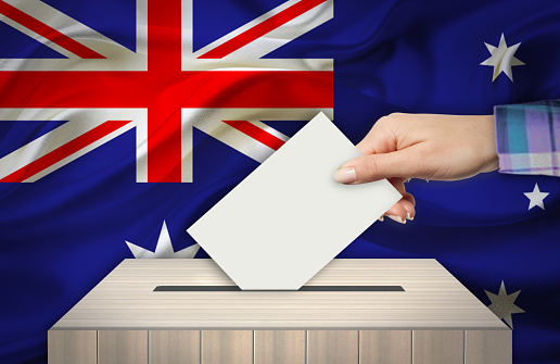 Hand with voting ballot and box in front of the flag AUSTRALIA
