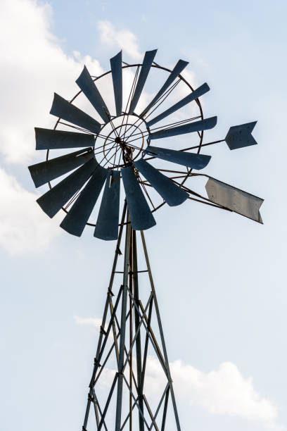istock Old-fashioned metal wind pump against pale blue sky with white clouds. 1142184208