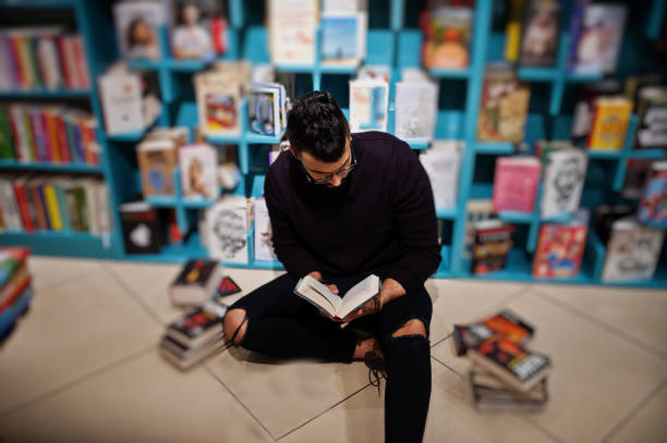 Smart arab student man in library Tall smart arab student man, wear on violet turtleneck and eyeglasses, at library sitting against books shelves. middle eastern ethnicity mature adult book reading stock pictures, royalty-free photos & images