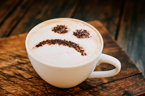 Cappuccino Coffee topped with a chocolate unhappy smiley face.