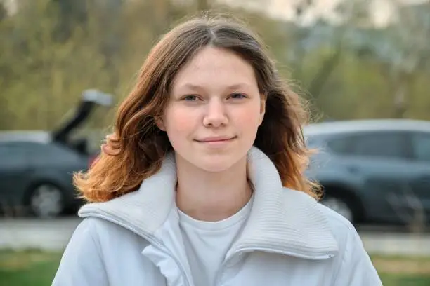 Photo of Outdoor portrait of teenager girl 15 years old, girl smiling with long brown hair in white jacket