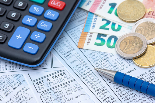 French payroll with social contributions and income tax deduction, mandatory in France since January 2019, along with a calculator, a pen, and euro coins and bank notes