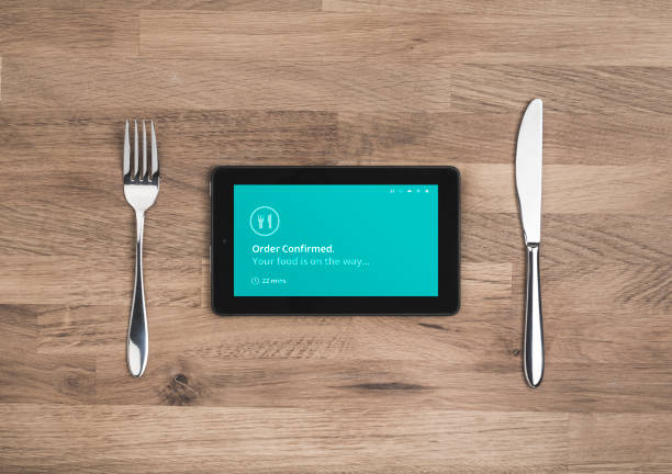 Online food order confirmation screen on mobile tablet with knife and fork on wooden table top.