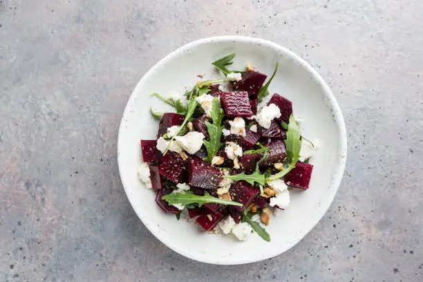 beetroot salad with blue cheese, arugula and walnut in a white plate on gray background, top view