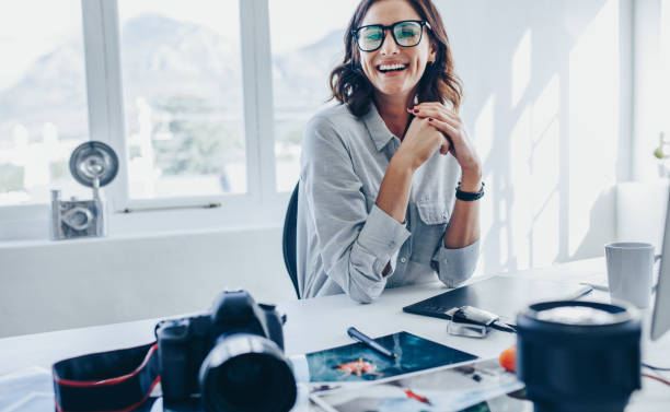 Female photo editor sitting at her desk Female photo editor sitting at her desk. Female photographer looking at camera and smiling in her office. graphic designer photos stock pictures, royalty-free photos & images
