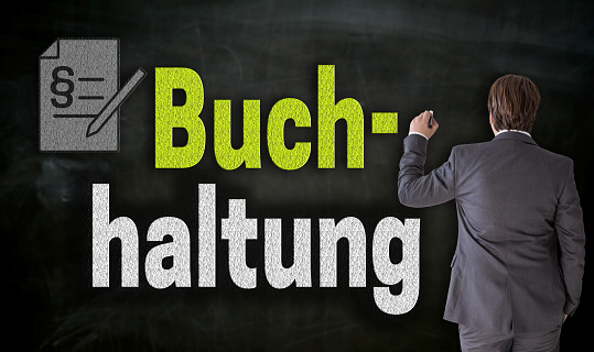 Businessman is writing with chalk Buchhaltung (in german accounting) on blackboard.