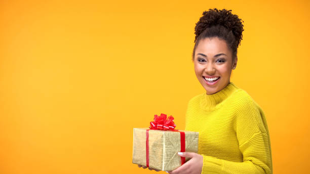 istock Joyful afro-american female holding present on bright background, happiness 1142207505