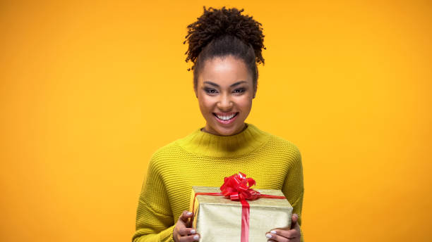 istock Young woman smiling on camera holding present in hands, holiday celebration 1142207509