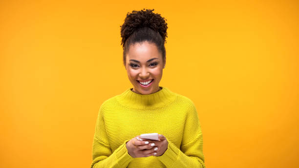 возбужденная афро-американская леди улыбается на камеру телефонной руки, сообщение в социальной сети - tone dialing стоковые фото и изображения