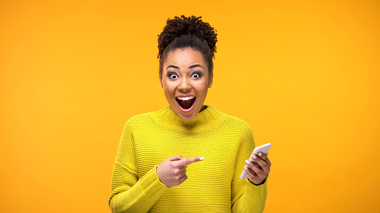 Joyful young woman pointing at smartphone in hand, online shopping application