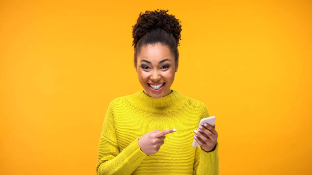 podekscytowana kobieta wskazująca telefon komórkowy w ręku, dobra wiadomość, komunikacja w sieciach społecznościowych - message communication sign african descent zdjęcia i obrazy z banku zdjęć