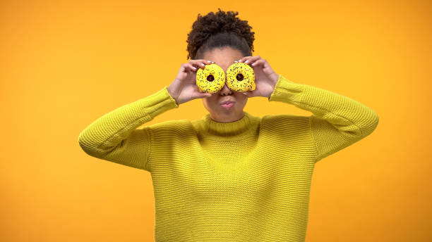 istock Cheerful Afro-American girl closing eyes with donuts, having fun, background 1142208525