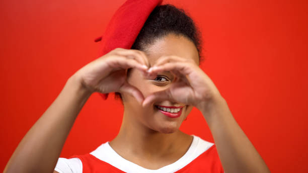 lächelnde frau, die herzzeichen von händen auf rotem hintergrund, freundlichkeit, nächstenliebe macht - human cardiovascular system heart shape human hand healthy lifestyle stock-fotos und bilder