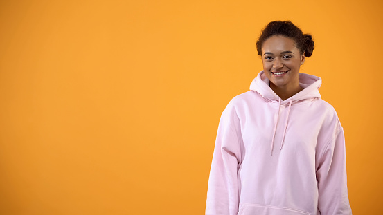 Teenage afro-american female in over-sized hoodie on orange background, fashion