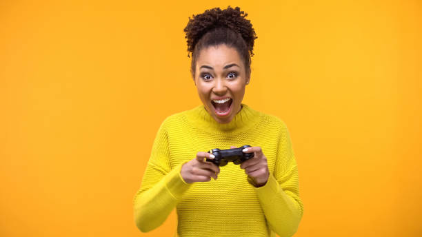 istock Happy female student with game joystick yellow background, hobby excitement 1142209397