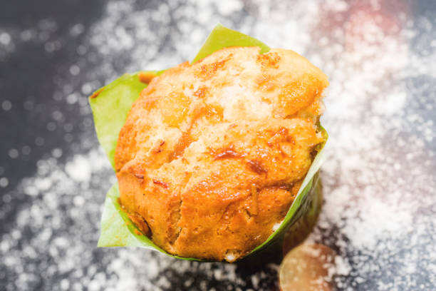 Chocolate muffin with raisin and almond slice on top. The muffin has a brown cover paper and placed in a row arrangement. It display above a white plate.