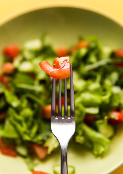 Fresh salad with cucumber and tomato, arugula in a green plate with fork