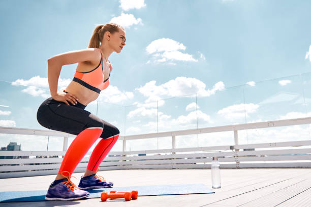 istock Motivated woman is doing squats on sunny terrace 1142217021