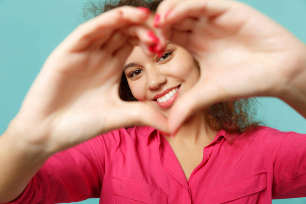 Portrait of smiling african girl in casual clothes showing shape heart with hands isolated on blue turquoise wall background in studio. People sincere emotions, lifestyle concept. Mock up copy space retrato de chica africana sonriente en ropa casual mostrando el corazón de forma con las manos aisladas en el fondo azul turquesa de la pared en el estudio. personas emociones sinceras, concepto de estilo de vida. mock up espacio de copia.