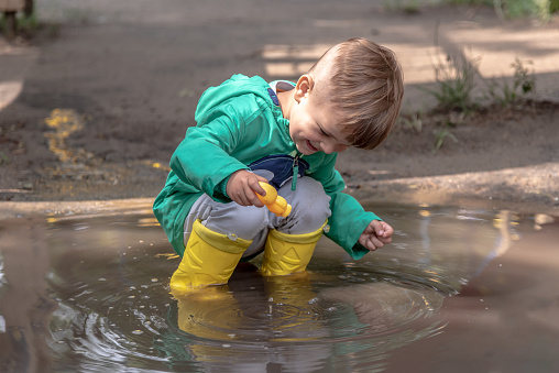 little boy playing sitting in a puddle in the park