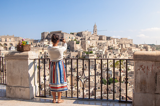Young elegant woman tourist in historical Matera town in Italy taking photos with smartphone