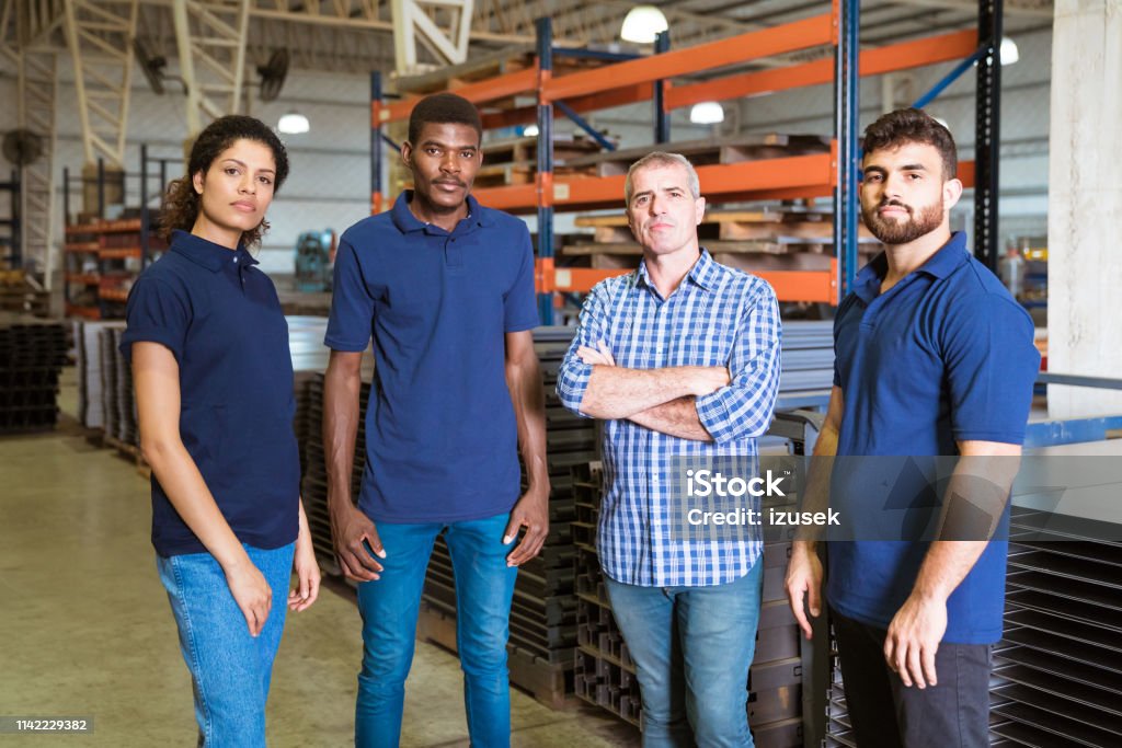 Confident workers standing in factory Portrait of instructor and apprentices in industry. Confident engineer is standing with trainees. They are in factory. 20-24 Years Stock Photo