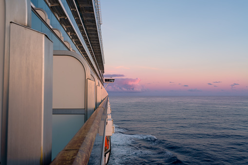 View of the starboard side of a cruise ship at sunset in the Caribbean Sea. Pink skies and ocean in the background