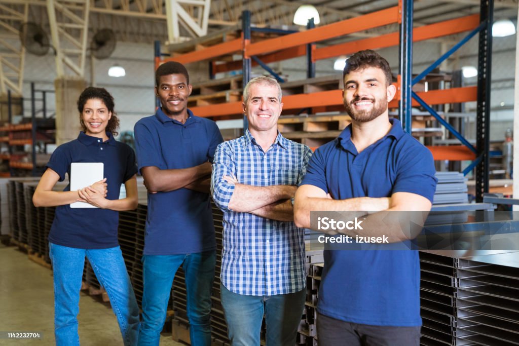 Smiling confident workers standing in industry Confident multi-ethnic workers in factory. Male engineer is standing with trainees. They are with arms crossed in factory. Arms Crossed Stock Photo