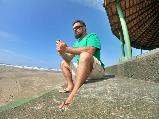 Man sitting on a beach looking at his smartphone