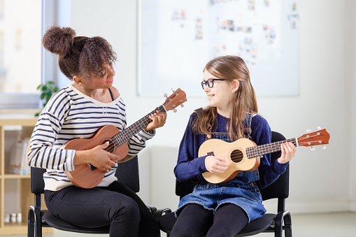 Young woman teaching girl playing the ukulele in the music school.