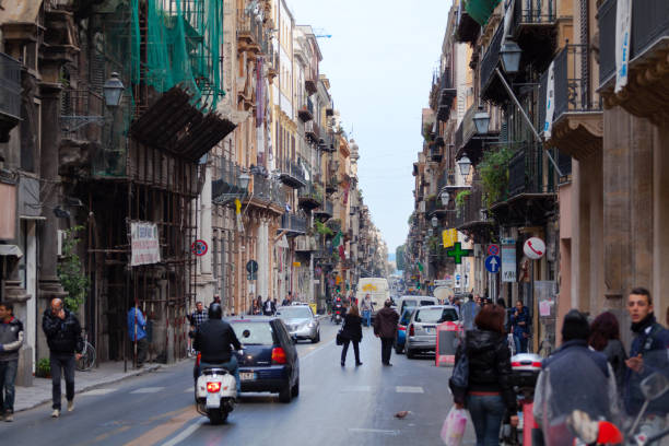 View along street Via Vittorio Emanuele in Palermo with rowhouses. Some traffic is on street. People are walking on sidewalks.