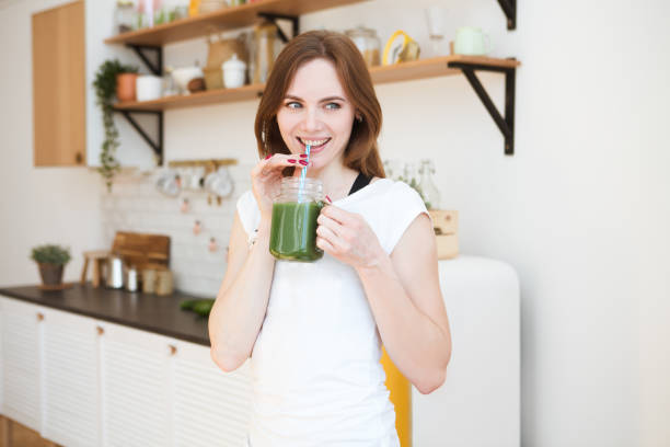 웃는 젊은 여자 부엌에서 녹색 스무디 주스를 마시는. 건강 한 라이프 스타일. - chlorella 뉴스 사진 이미지