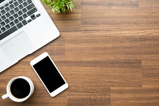 istock Wood office desk table with smartphone with blank screen, laptop and coffee cup. Top view with copy space, flat lay. 1142238604