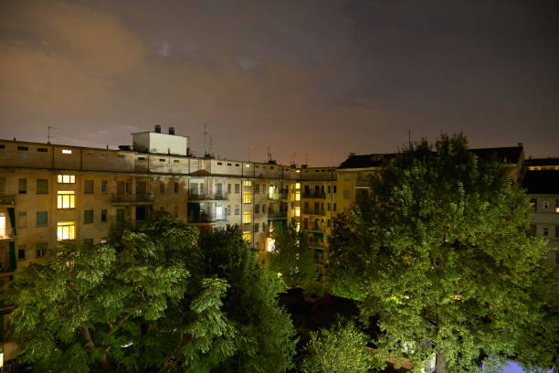 istock Buildings and green trees at night, illuminated cloudy sky 1142239038