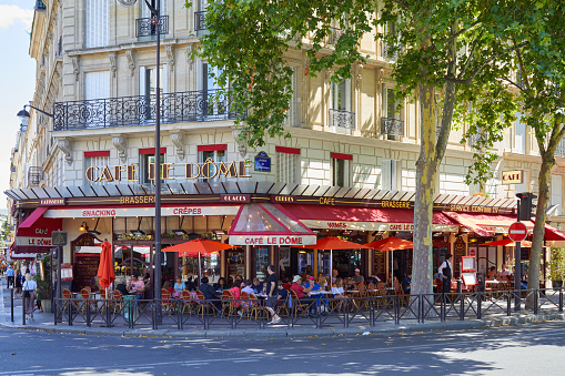Paris, France - July 21, 2017: Typical cafe brasserie with sidewalk tables with people and tourists sitting in a sunny summer day in Paris, France