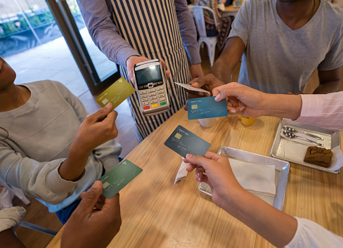 Close-up on a group of customers paying with a credit card at a restaurant and splitting the bill â business concepts. **DESIGN ON CARDS WERE MADE FROM SCRATCH BY US**
