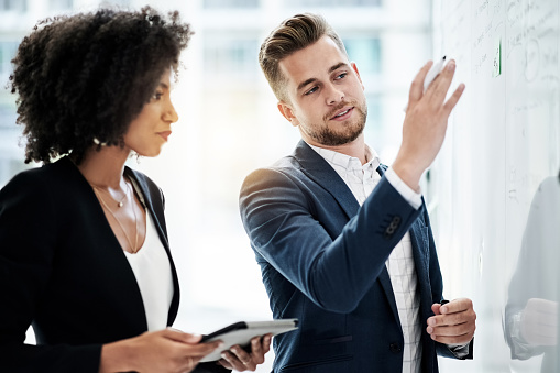 Cropped shot of two young businesspeople strategizing on a whiteboard in their corporate office