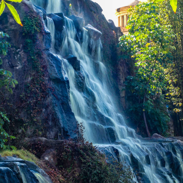 Wide wall with waterfall in a public nature park in Guadalajara Jalisco Mexico on a sunny day with a lake, trees, colorful flowers and lots of green vegetation