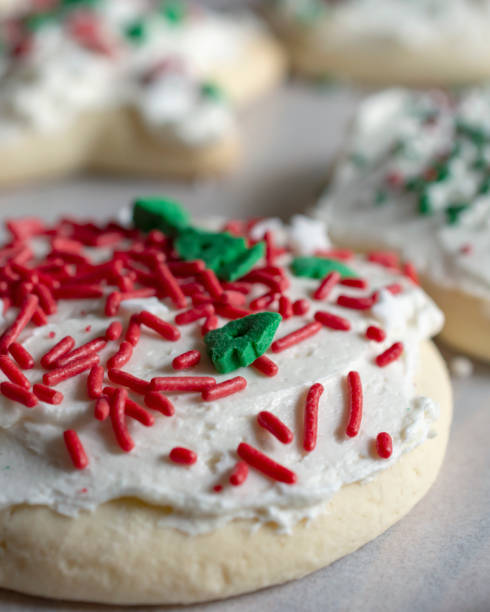 Round shaped sugar cookie with frosting and sprinkles. Additional varying sugar cookies in the background.  Close up side view. white sugar cookie stock pictures, royalty-free photos & images